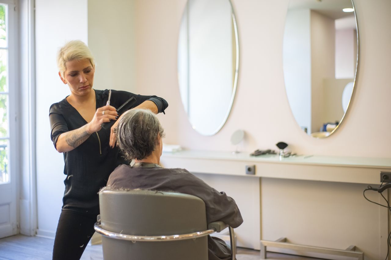 A hairdresser skillfully cuts an elderly woman's hair in a modern salon with mirrors and a comfortable barber chair.